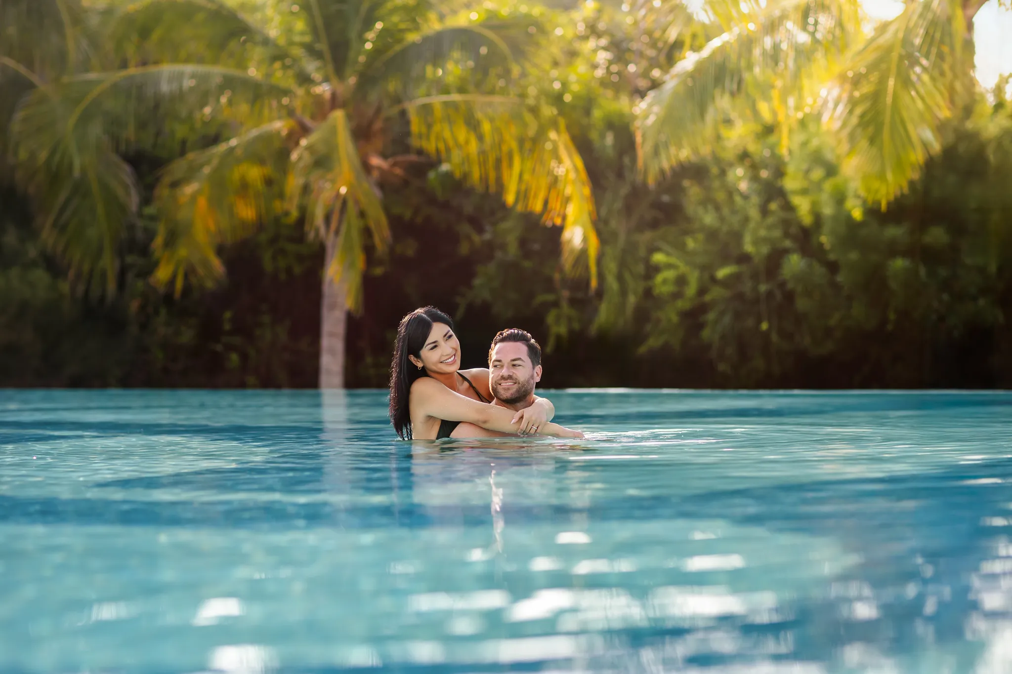 Couple embracing in a tranquil pool surrounded by palm trees at Secrets Huatulco Resort & Spa, enjoying a romantic adults-only escape.