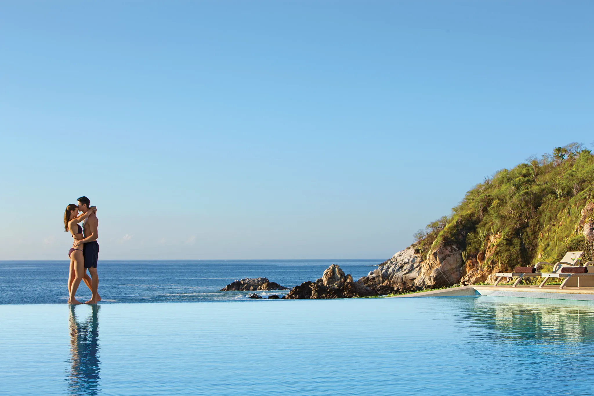 Couple standing at an infinity pool overlooking the Pacific Ocean at Secrets Huatulco Resort & Spa during a romantic getaway.
