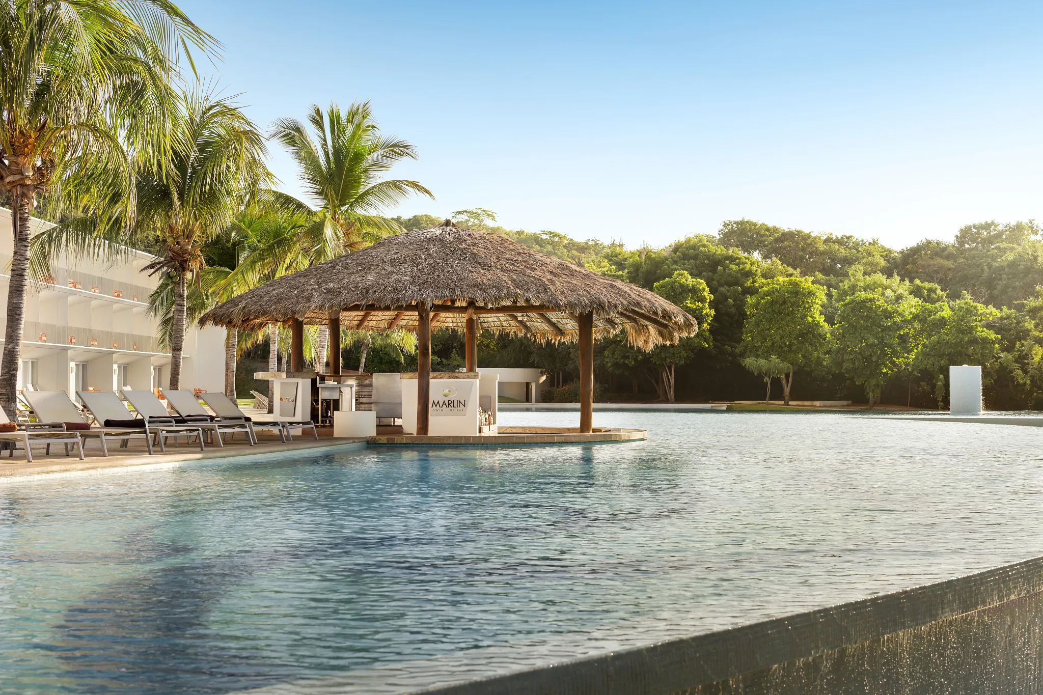 Marlin swim-up bar at Secrets Huatulco Resort & Spa featuring a thatched-roof in-pool bar, tropical cocktails, and palm-lined pool setting.