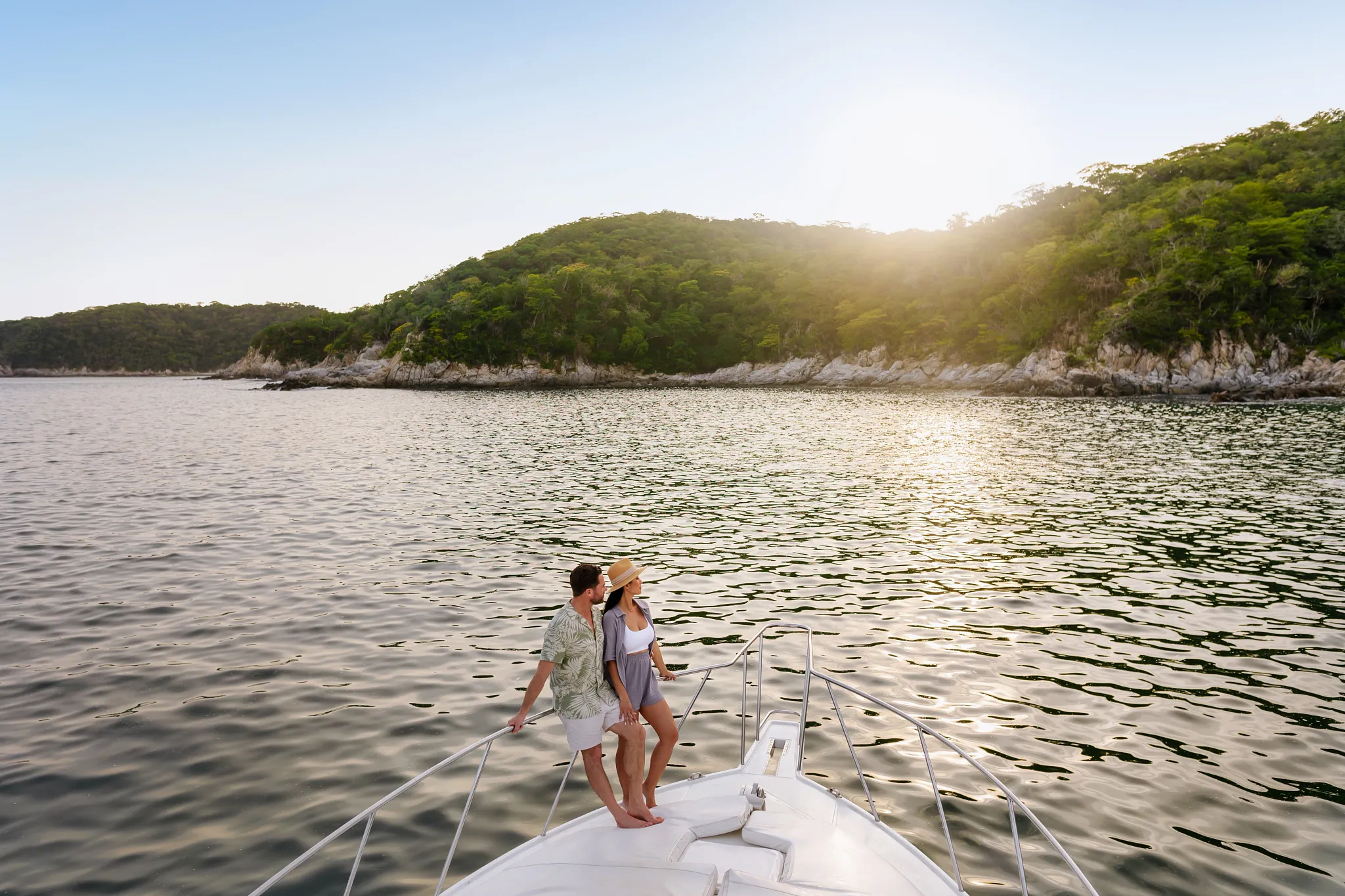 Couple relaxing on a luxury catamaran during sunset near Secrets Huatulco Resort & Spa, overlooking calm waters and forested coastline.