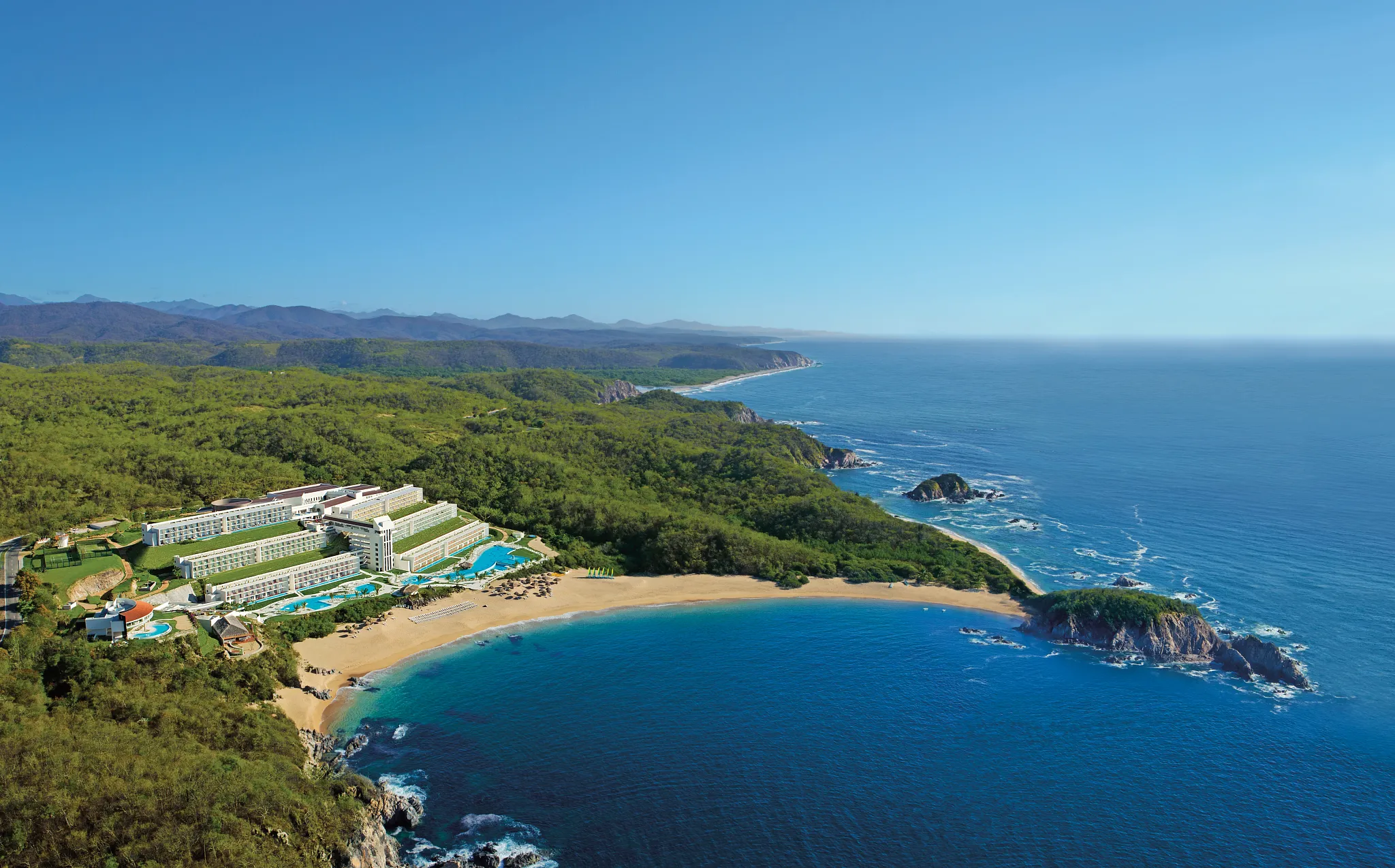 Panoramic aerial view of Secrets Huatulco Resort & Spa nestled between lush jungle and the Pacific Ocean.