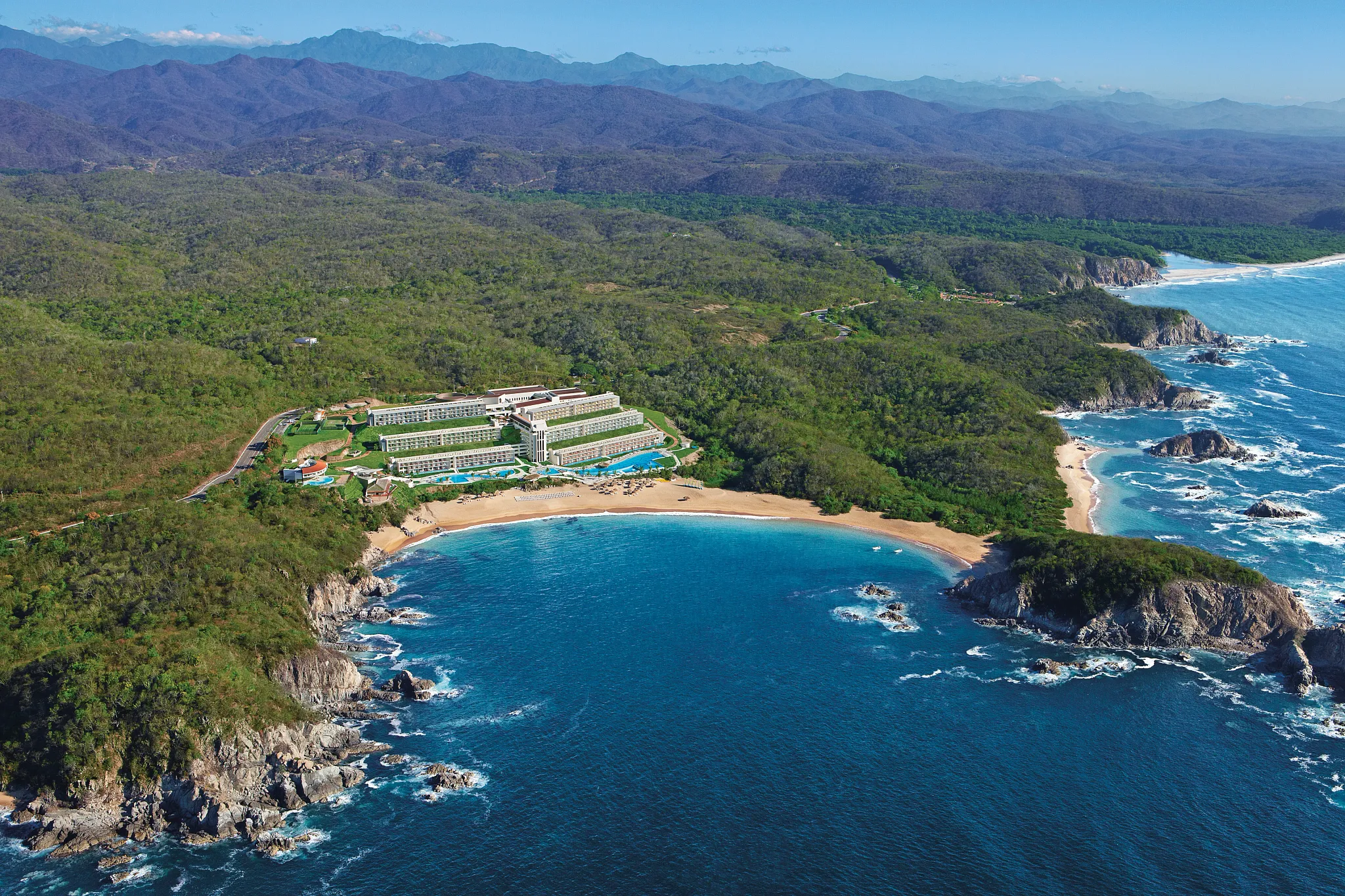 Aerial view of Secrets Huatulco Resort & Spa nestled between lush mountains and a secluded bay along the Pacific coast of Mexico.
