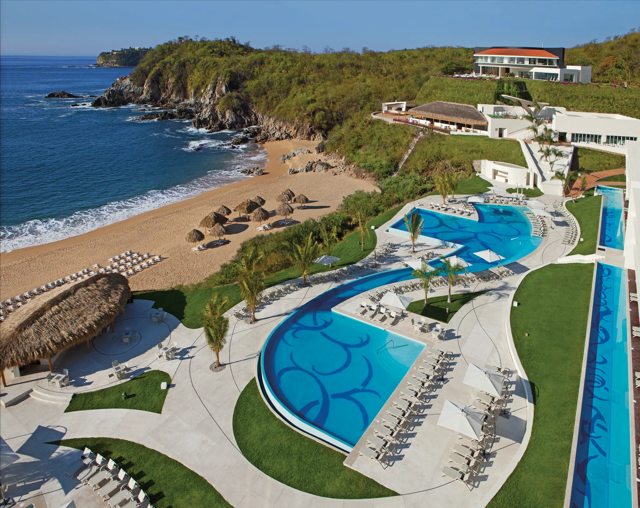 Aerial view of beachfront pools and sandy shore at Secrets Huatulco Resort & Spa, an adults-only luxury resort in Huatulco, Mexico.