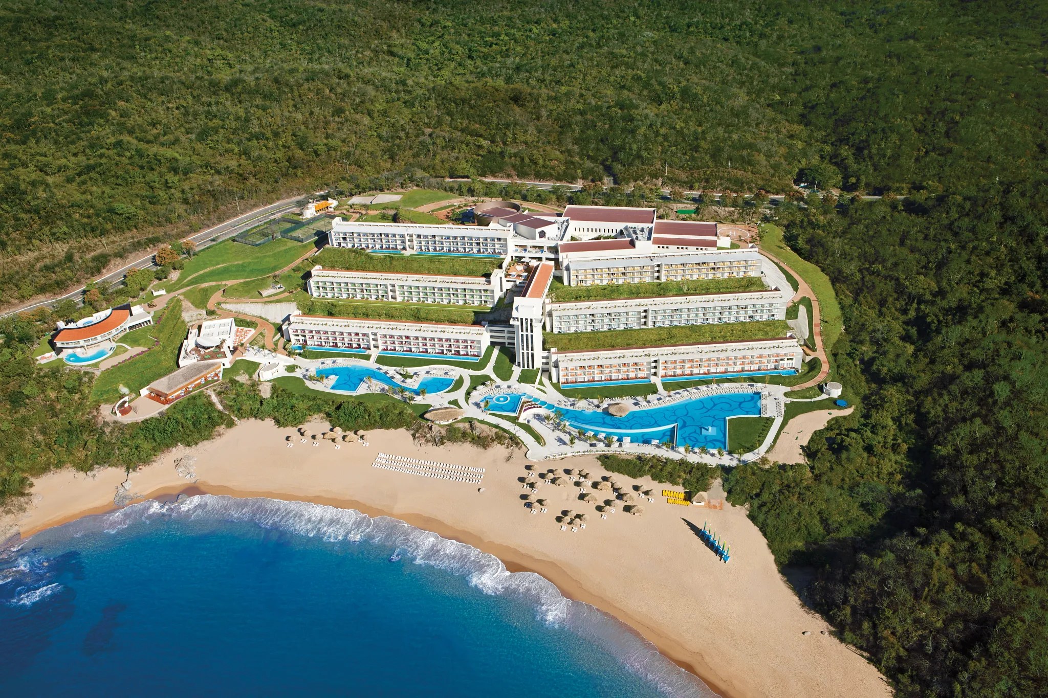 Overhead view of Secrets Huatulco Resort & Spa featuring infinity pools, beachfront loungers, and lush tropical landscaping.