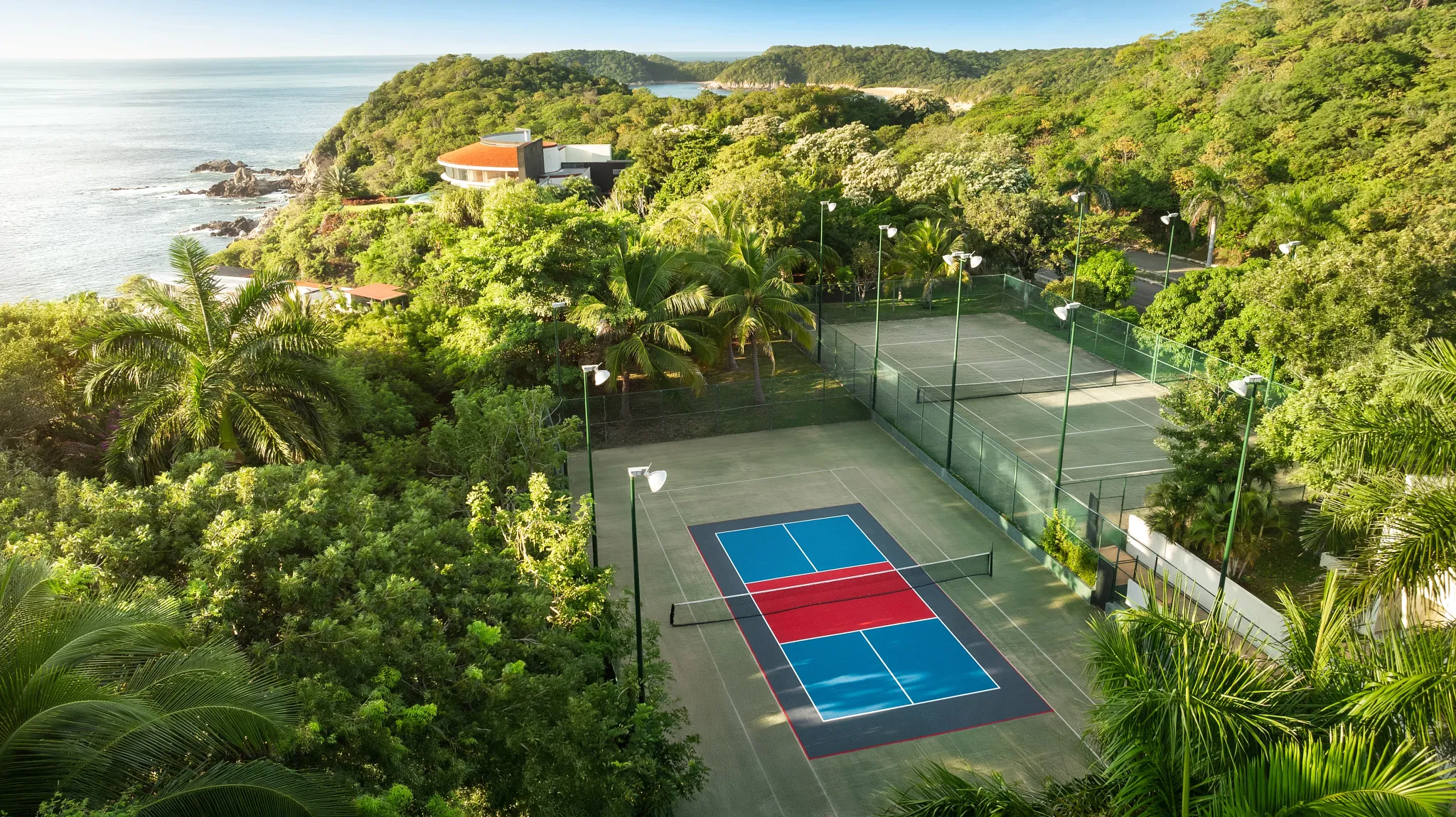 Aerial view of tennis courts surrounded by tropical jungle at Secrets Huatulco Resort & Spa along the Pacific coast.