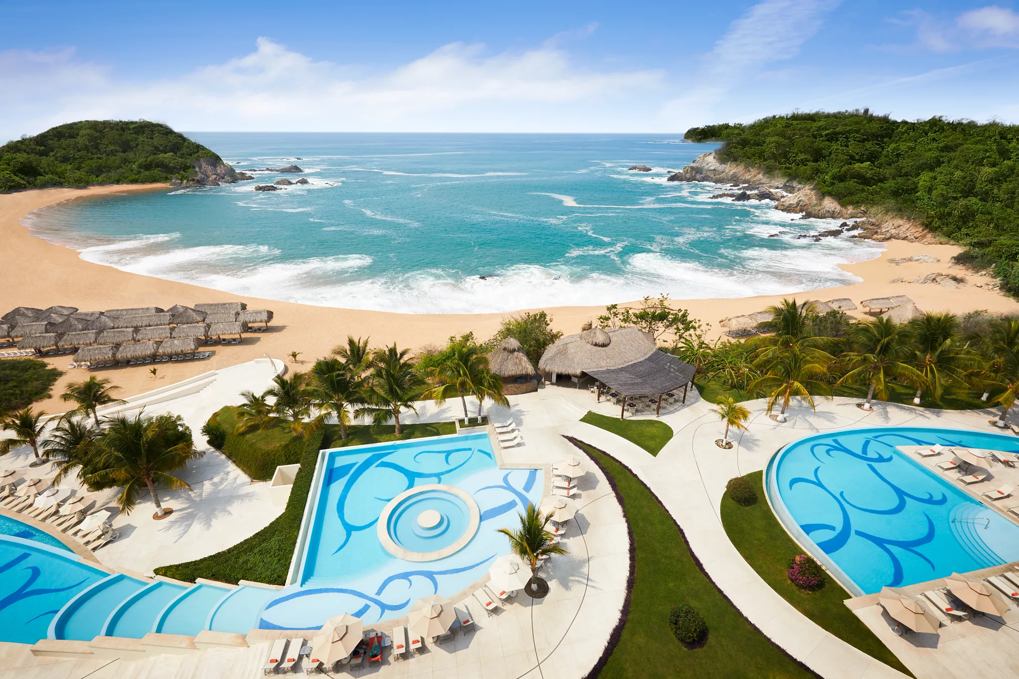 Aerial view of oceanfront pools and beach at Secrets Huatulco Resort & Spa with palm-lined pathways.