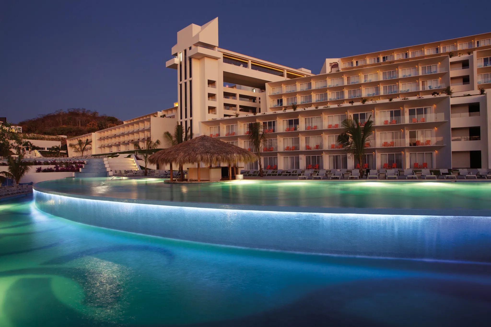 Illuminated infinity pool at night at Secrets Huatulco Resort & Spa, creating a romantic adults-only evening ambiance.