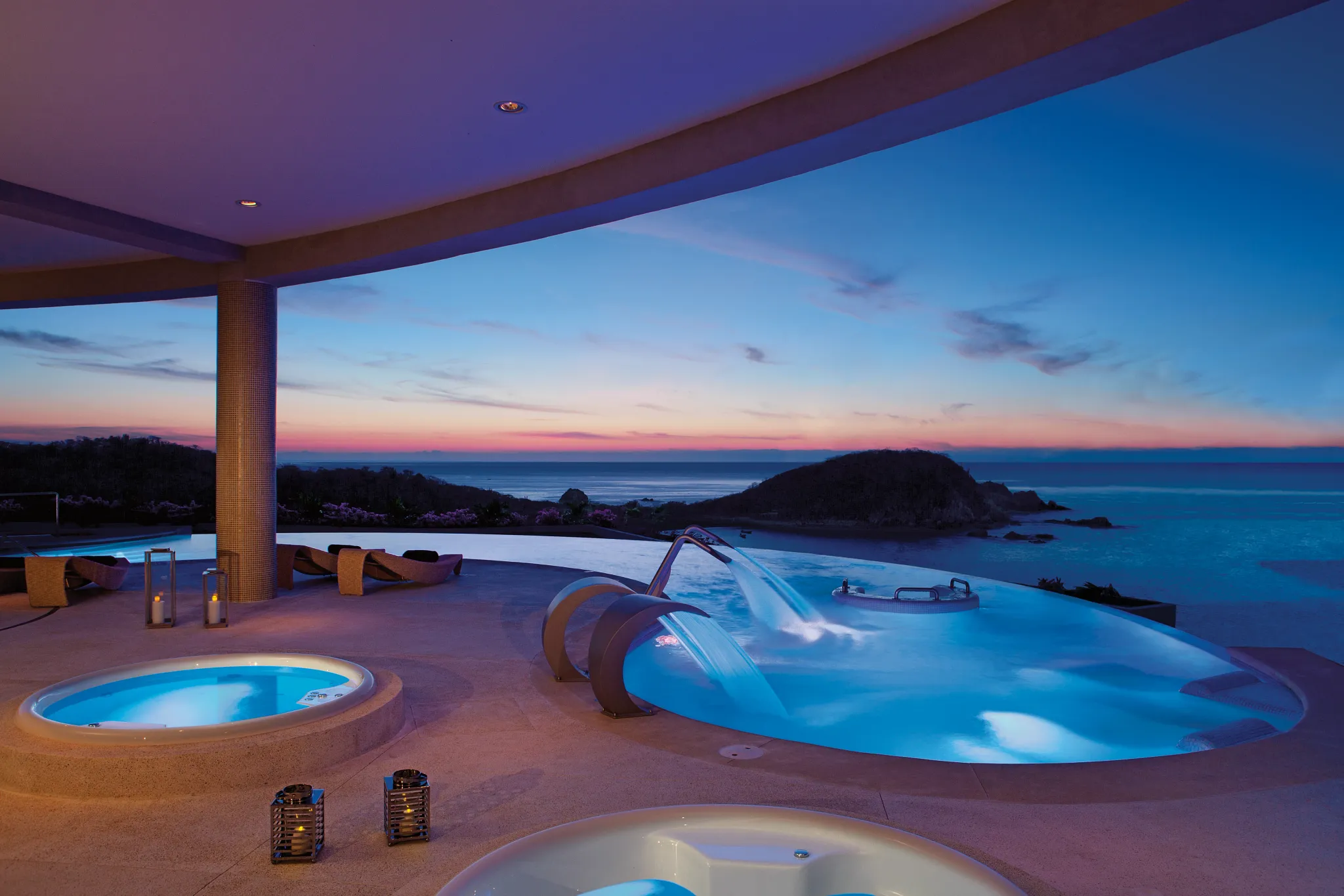 Illuminated spa circuit pools at night with ocean views at Secrets Huatulco Resort & Spa.