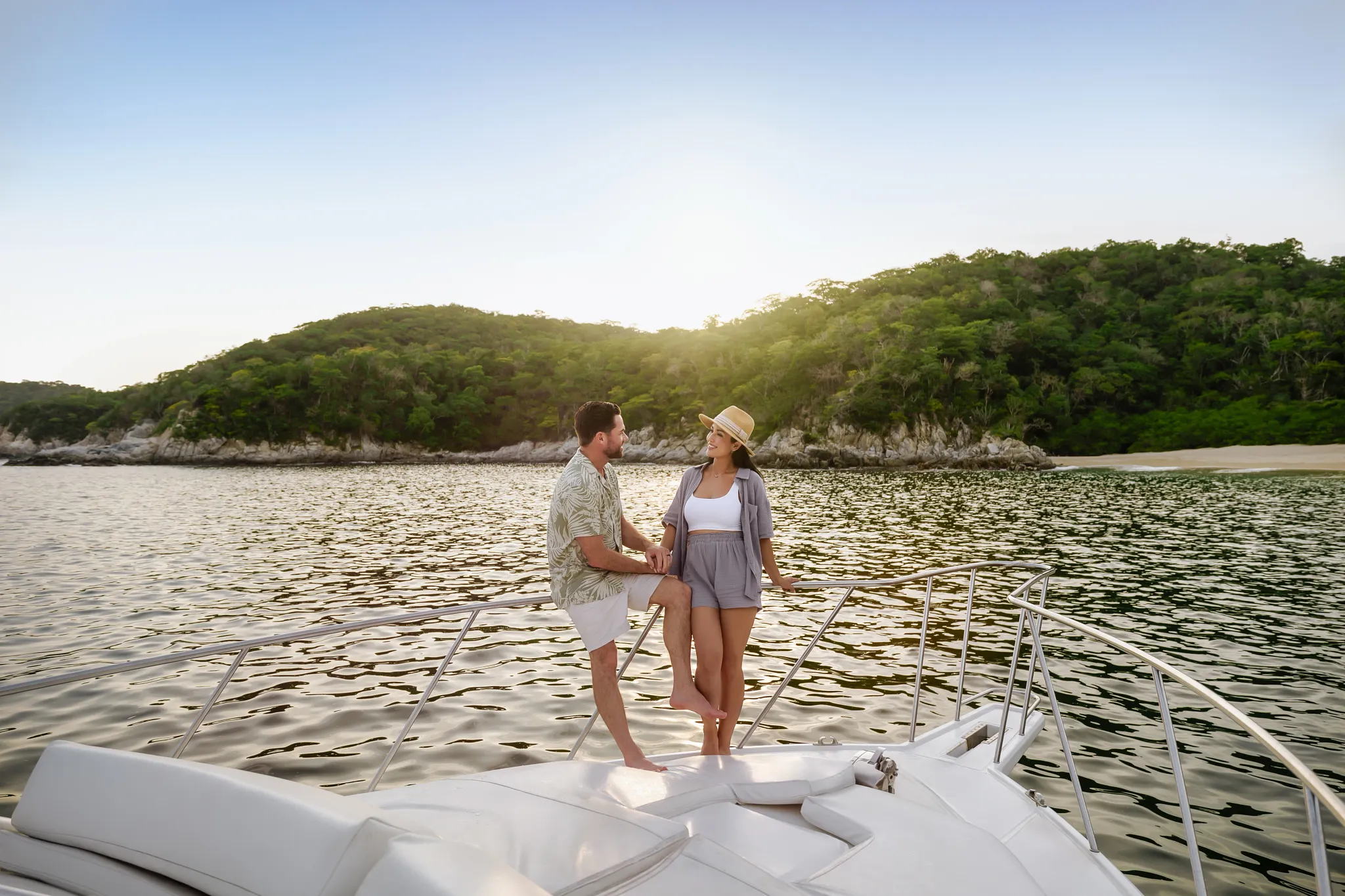 Couple relaxing on a luxury catamaran during sunset near Secrets Huatulco Resort & Spa, overlooking calm waters and forested coastline.
